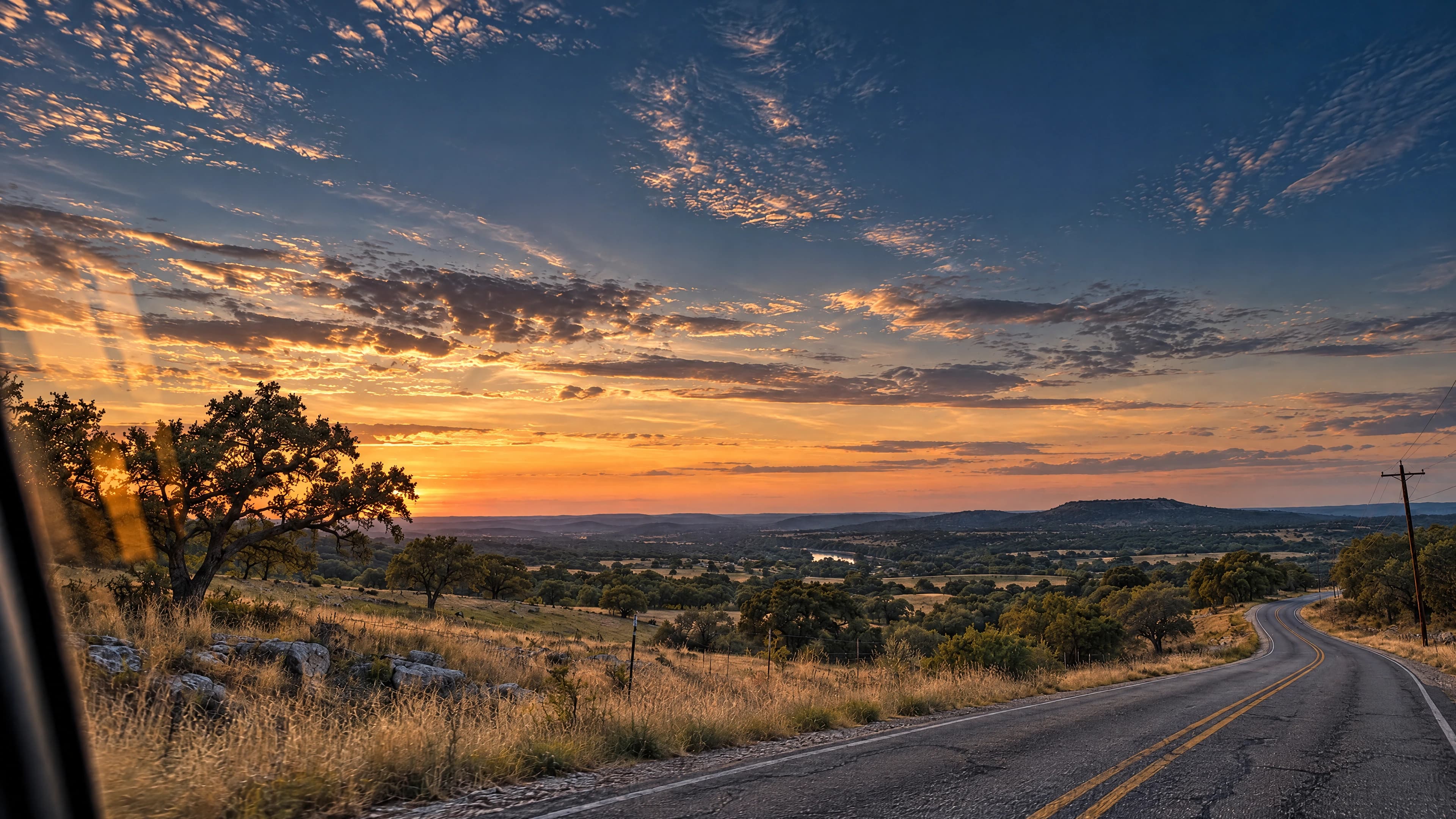 A winding two-lane road through the Hill Country at sunset, seen from inside a car.