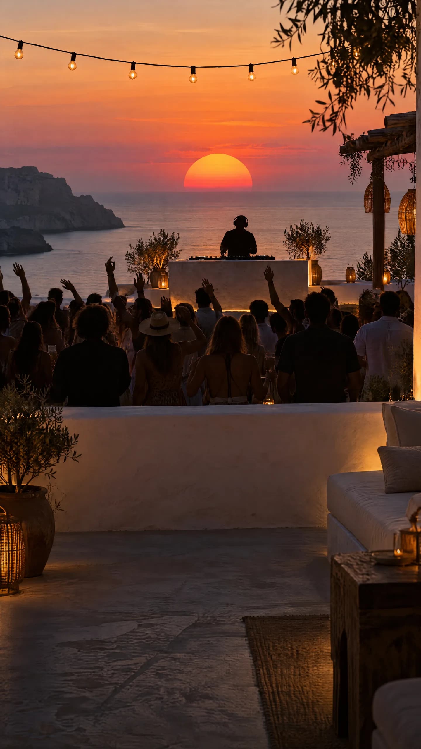 A white terrace above the sea in Ibiza at sunset, the crowd waving at the DJ as the sun goes down behind the booth
